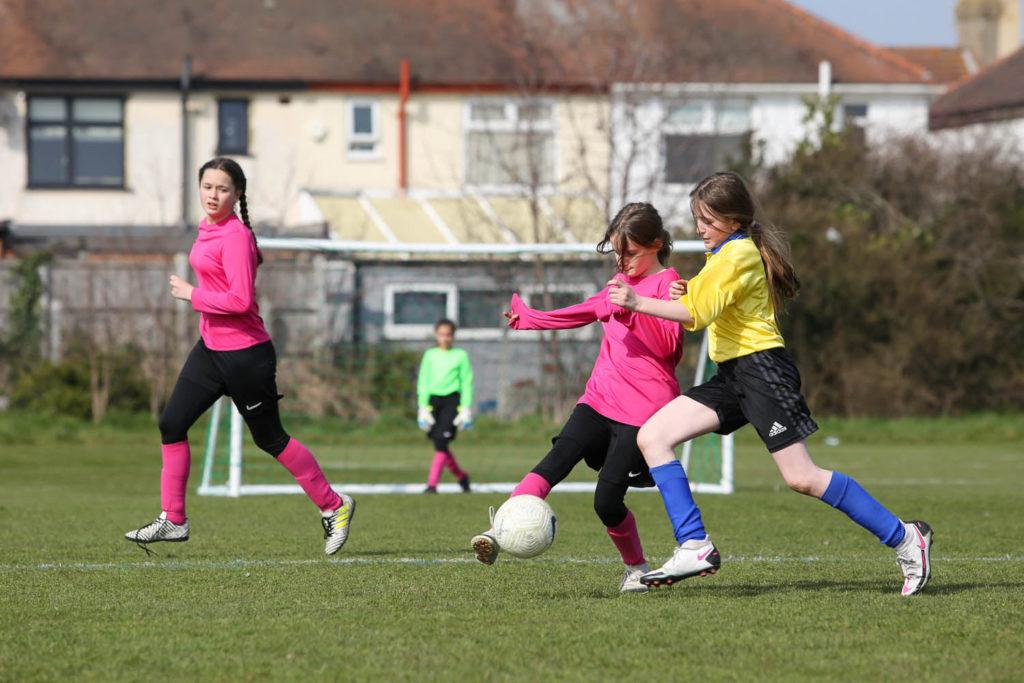 Young girls playing soccer on a grass field.