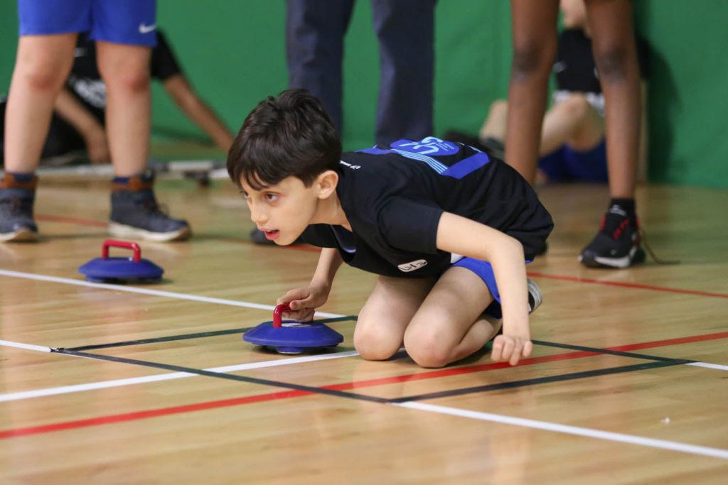 A young boy happily playing with a frisbee while kneeling on the floor.