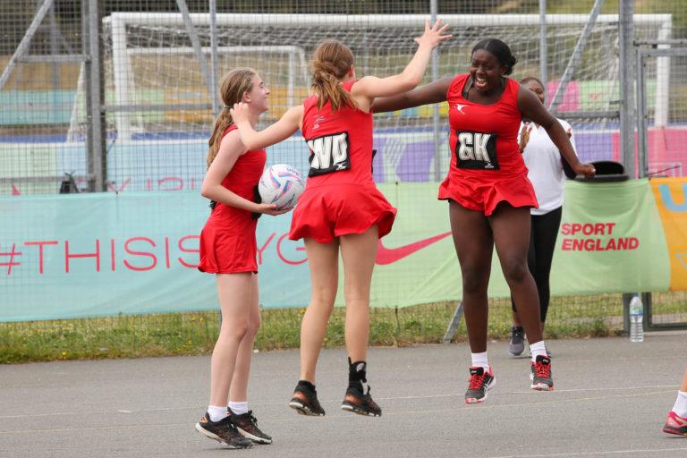 3 netballers celebrate a win, 2 white girls and 1 Black girl