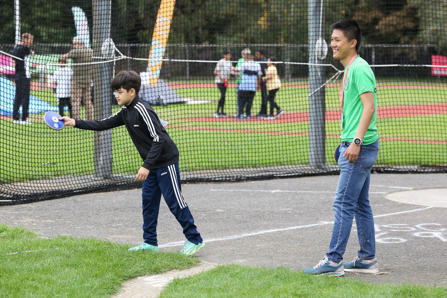 brown skinned boy throws discus and brown skinned male smiles