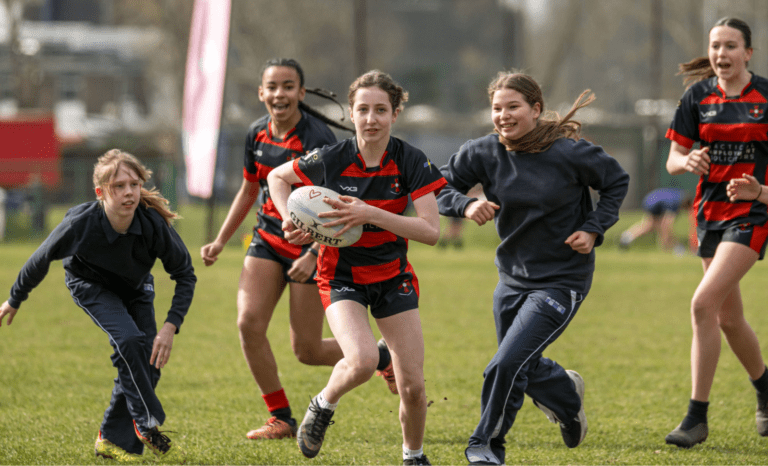 1 black female and 4 white females play rugby and smile